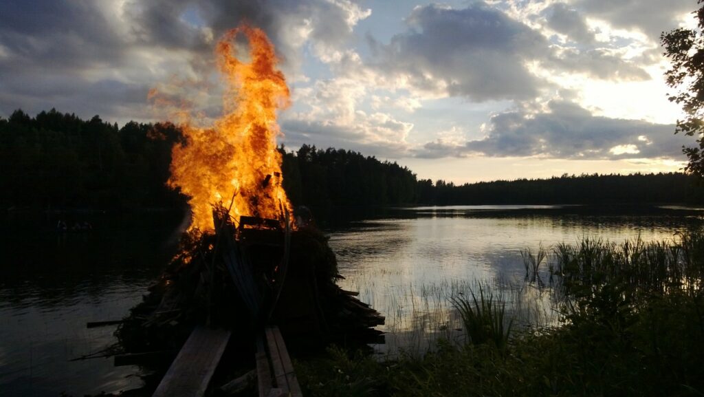 Kokko palaa pimenevässä illassa järven rannalla.