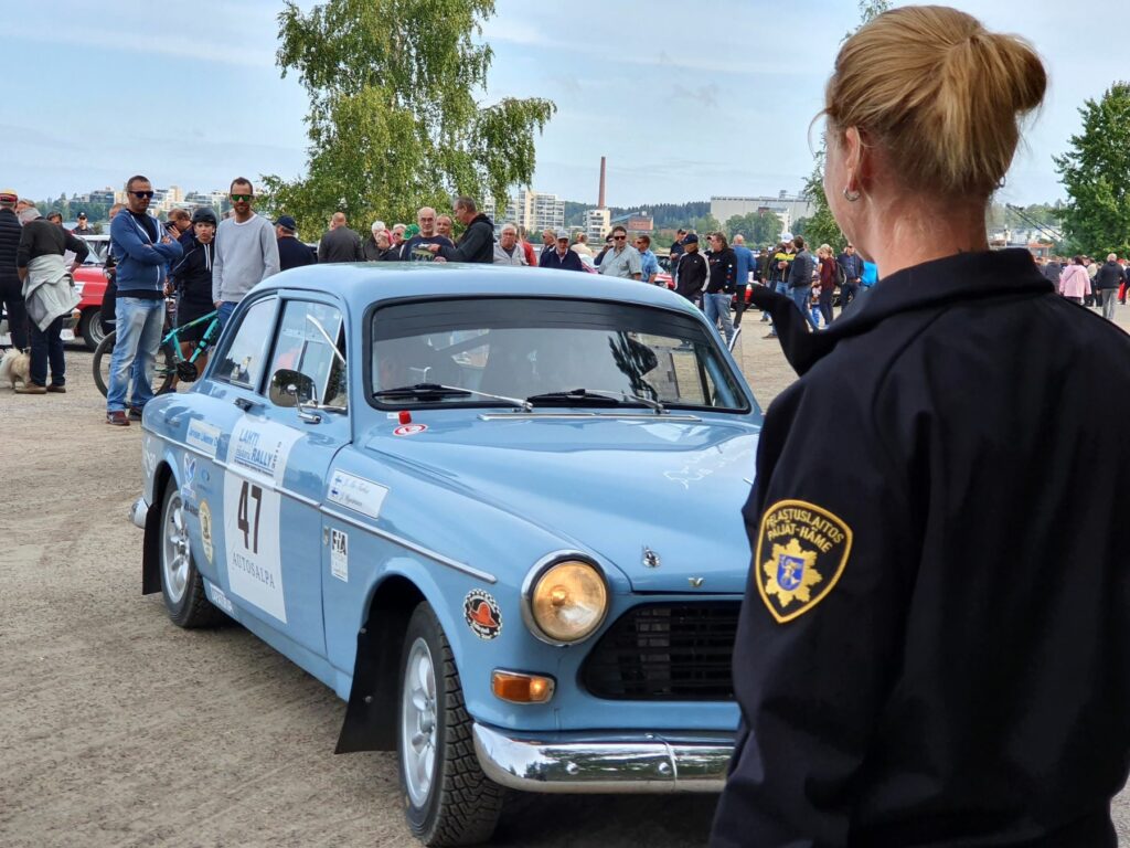 Siniseen virkapukuun pukeutunut palotarkastaja yleisötapahtumassa, jossa vanhoja autoja.