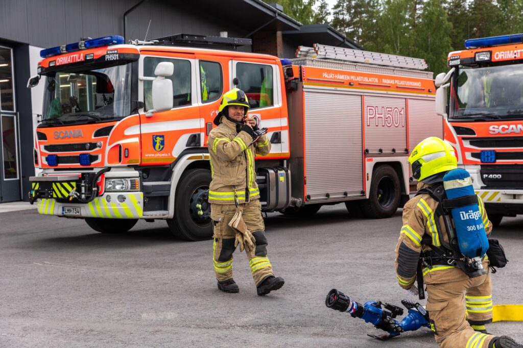 Paloauto PH501 sekä kaksi palomiestä pelastajan varusteissa ulkona valmistautumassa harjoitukseen.